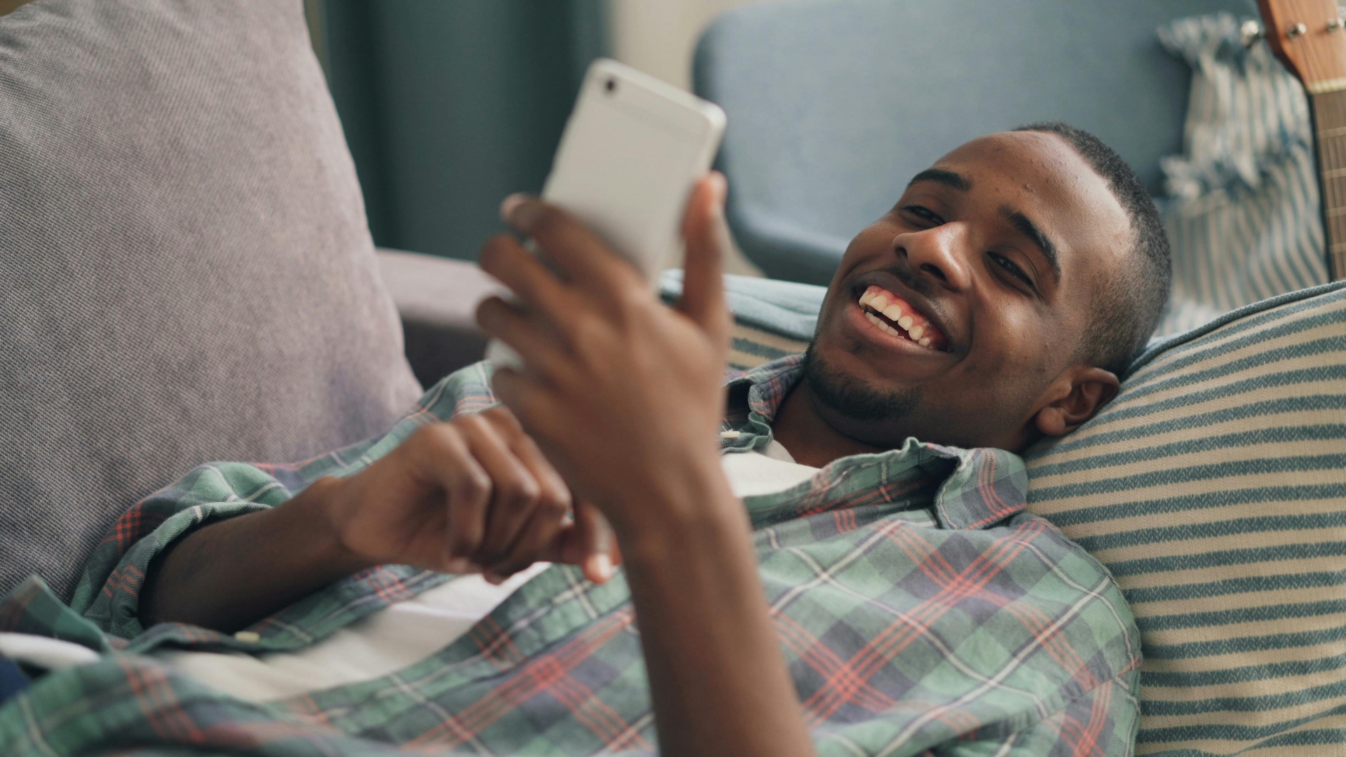A man looking at his phone while reclined and smiling